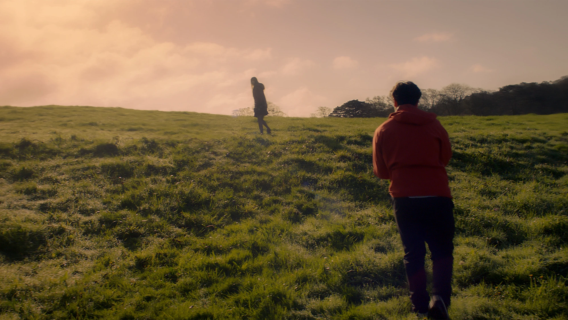 Courtney walking away across a sunlit field